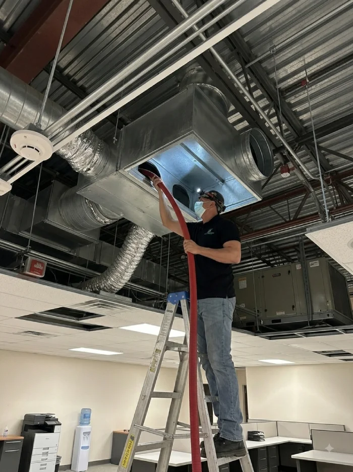 Commercial air duct cleaning technician servicing an HVAC duct system in an office building.