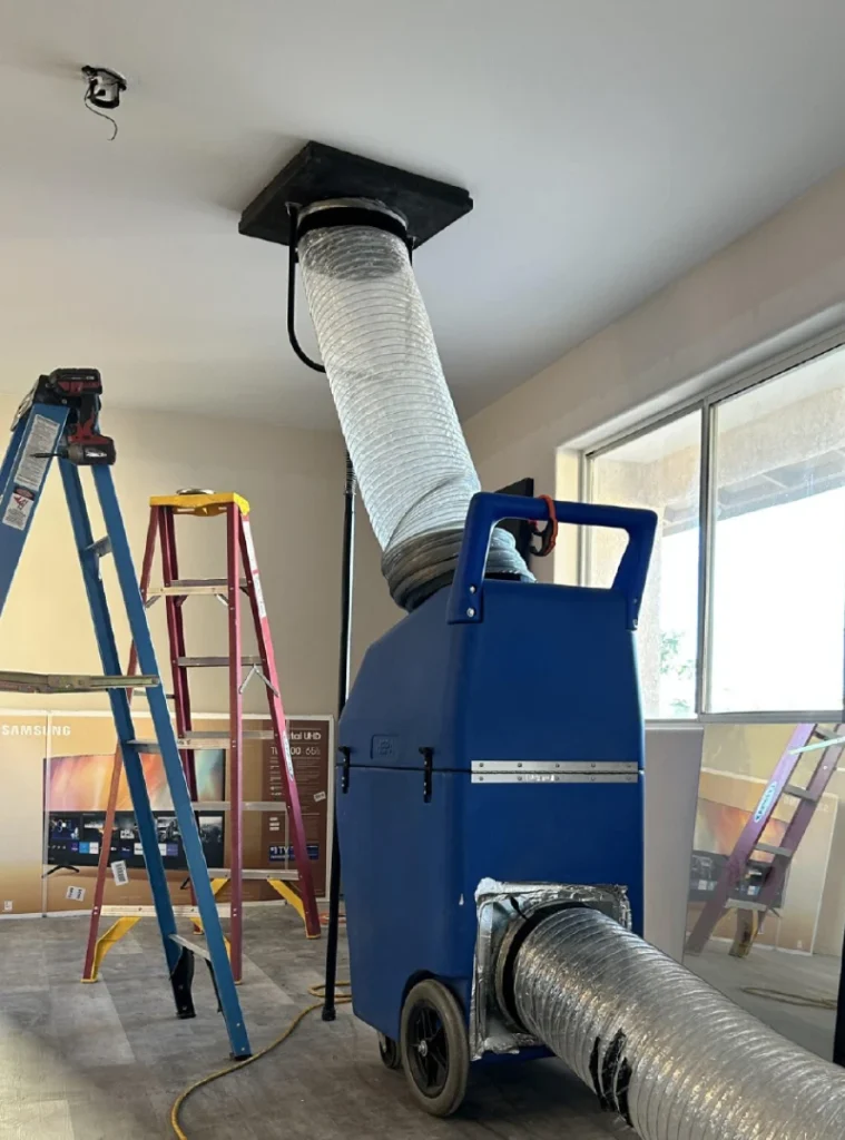 Commercial air duct cleaning equipment connected to a ceiling HVAC system in an office interior.