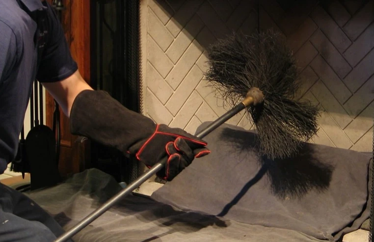 Chimney technician using a professional wire brush to clean the interior of a fireplace chimney.